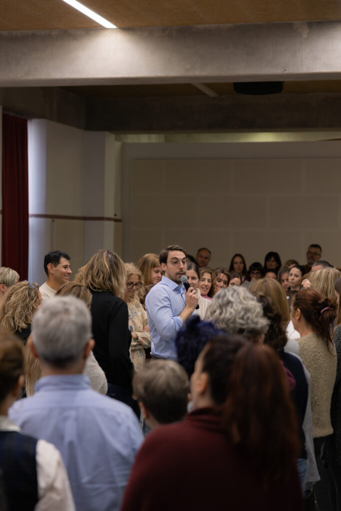 Facilitador conduint una dinàmica participativa amb un grup nombrós de professionals durant una sessió de lideratge i comunicació.